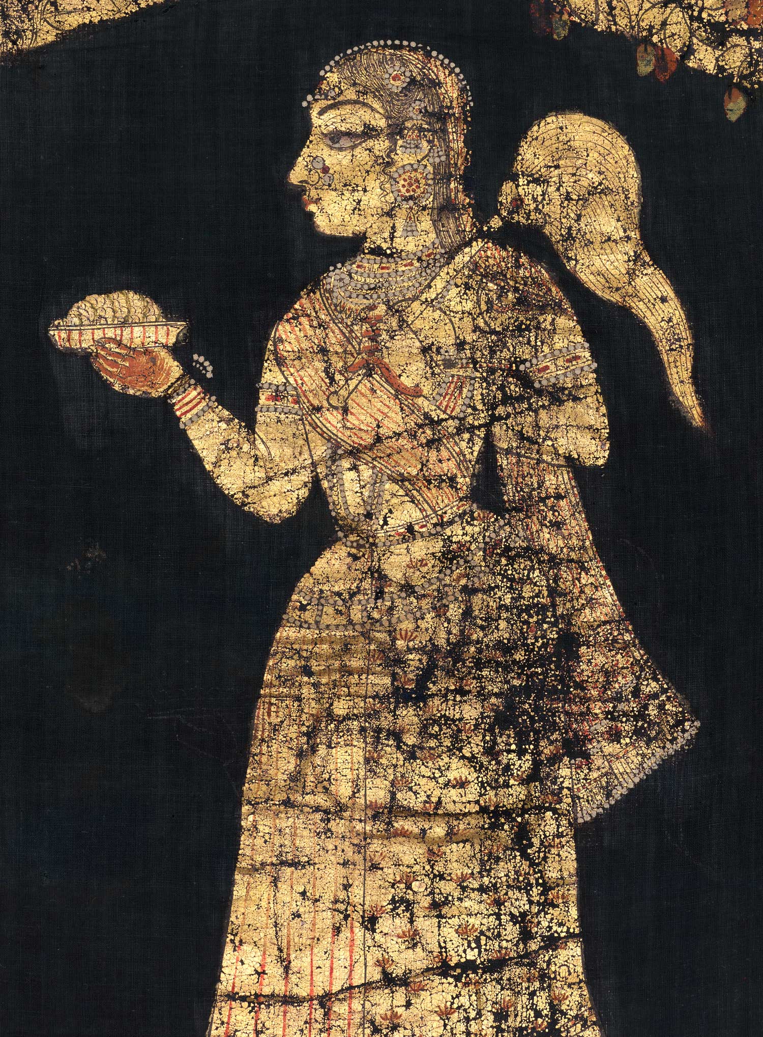 A gold woman facing left offers a plate of food in her right hand and holds a fly-whisk over her left shoulder.