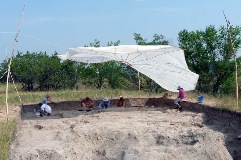 White parachute tented on poles over people digging.