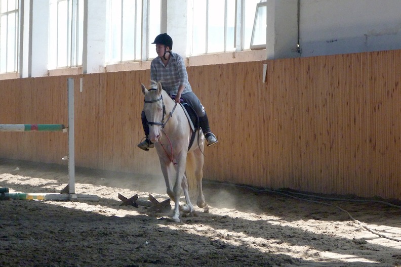 A rider on horseback in a dirt-floored building.
