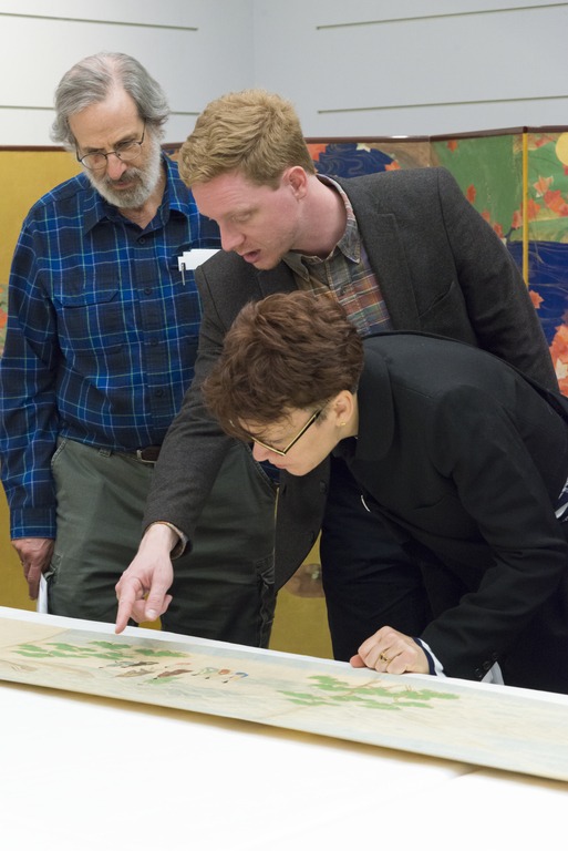 Three people looking at artwork on a table.