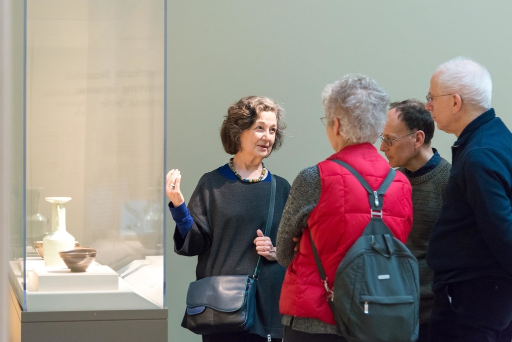 a woman standing near a display case in a gallery talking to three onlookers.