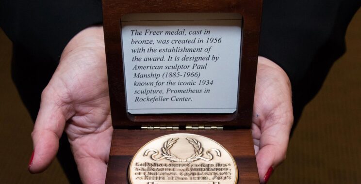 Hands holding a golden medal in a wooden box.