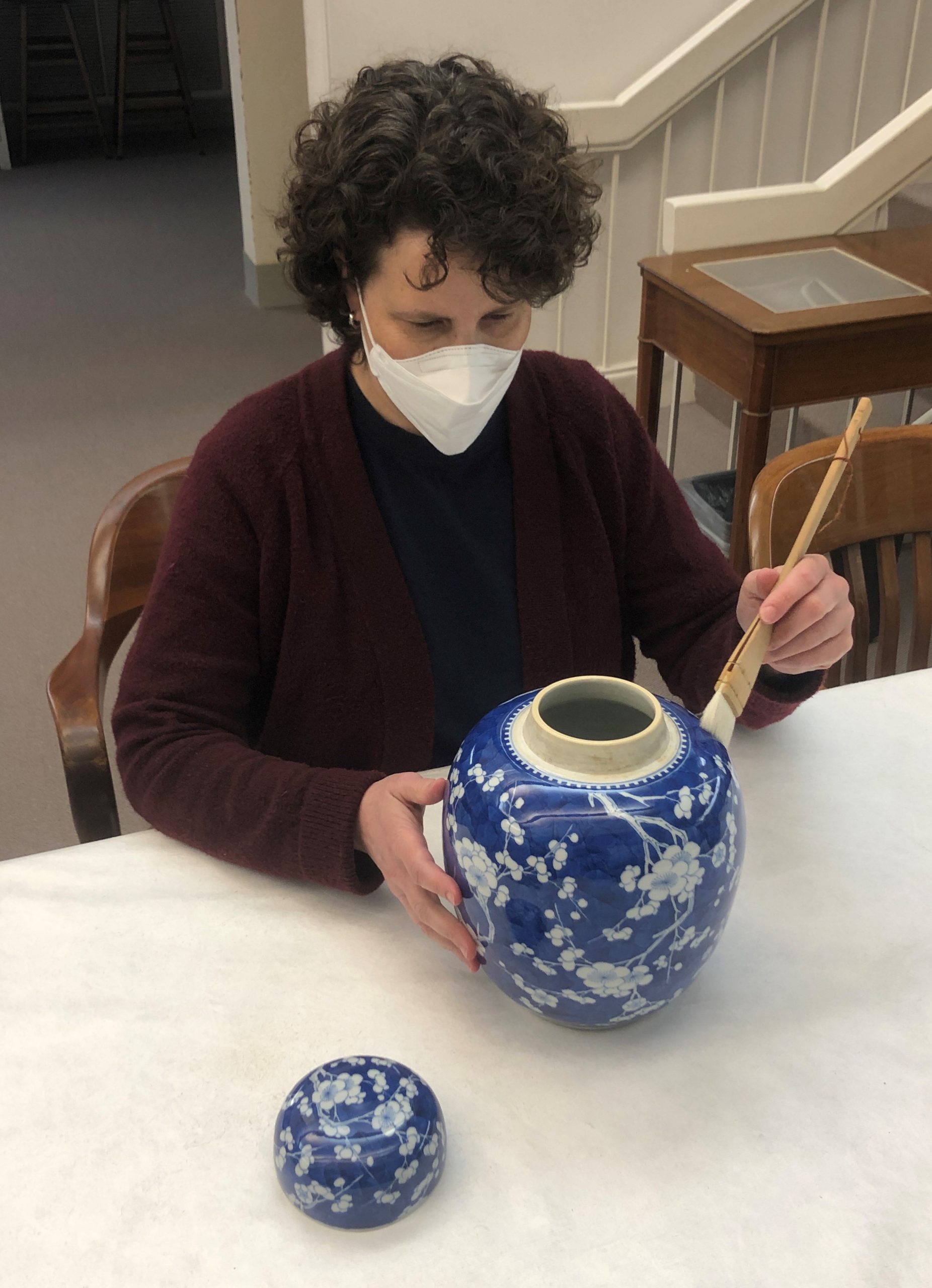 Conservator works on a blue and white ceramic vessel with a brush