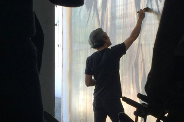 man works on a silvered surface with a brush.