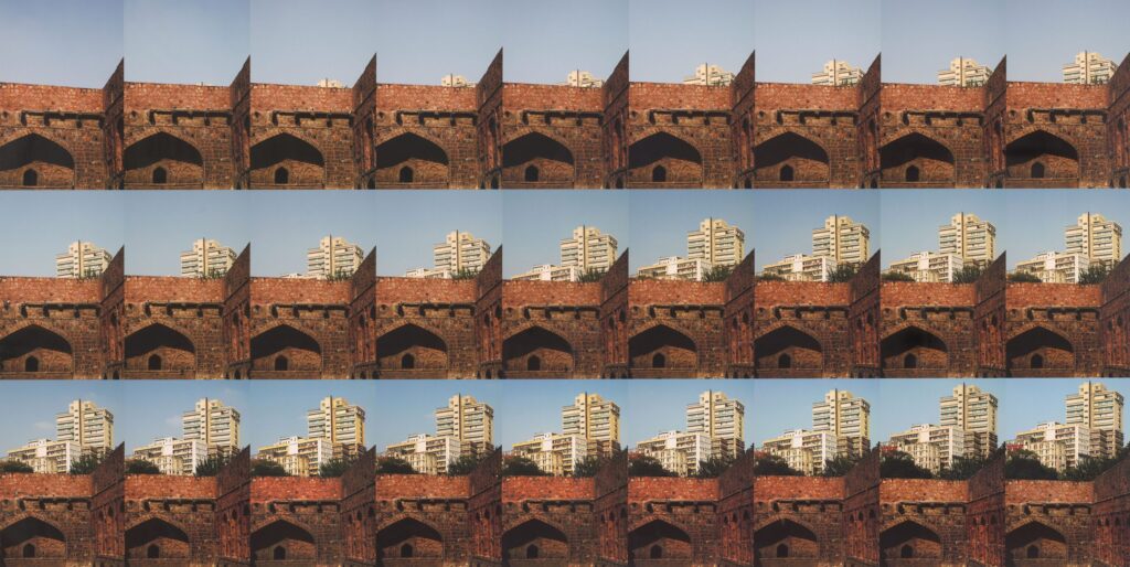 Twenty-seven photographs are arranged in a nine-by-three grid. In the background of each image is a blue sky, and in the foreground of each image is an old red brick wall. Read left to right, the images convey a narrative sequence. On the horizon line, cream-colored modern high-rise buildings appear to emerge upward step-by-step from behind the red brick.