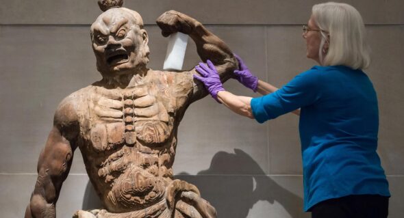 Conservator repairing the arm of a wooden guardian statue