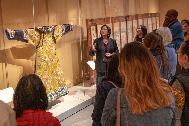 a curator lectures in front of an elaborate chinese robe.