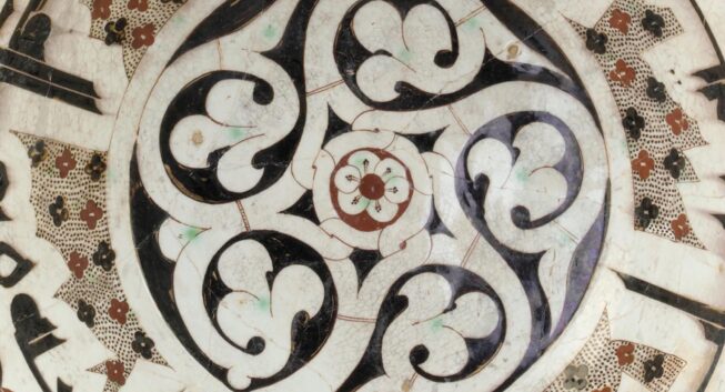 Detail, white ceramic bowl, painted with red and black floral designs with Arabic script around the edge