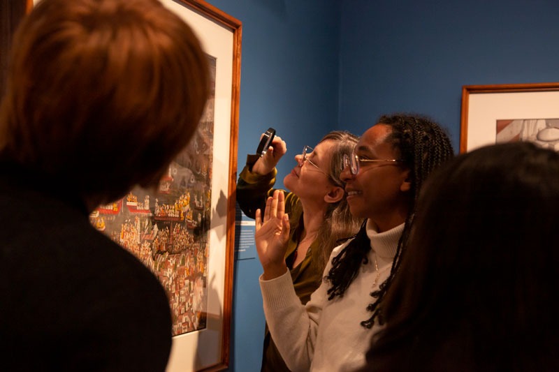 a group of visitors look closely at a painting, one with a magnifying glass