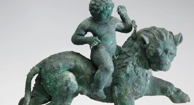 Bronze statue, with a green patina, of a child balancing astride a prancing, maned lion.