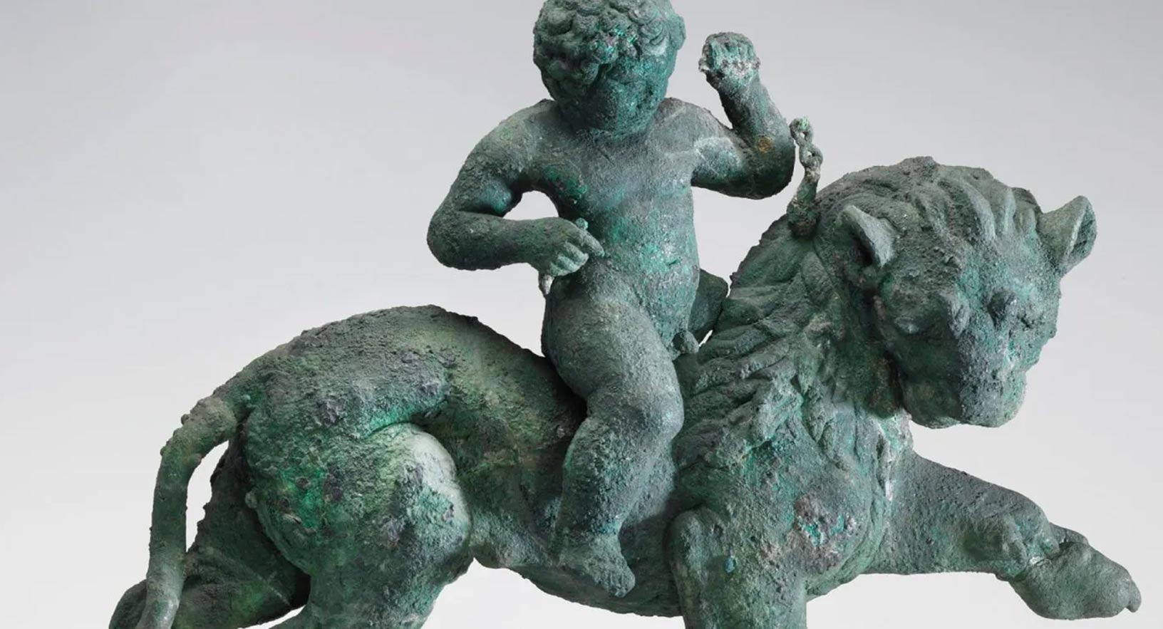 Bronze statue, with a green patina, of a child balancing astride a prancing, maned lion.