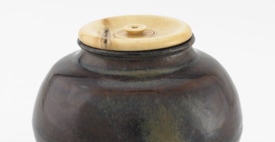 Small dark brown jar with a light tan lid.