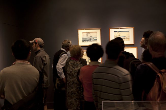 Visitors in dark gallery, looking at objects in pools of light.