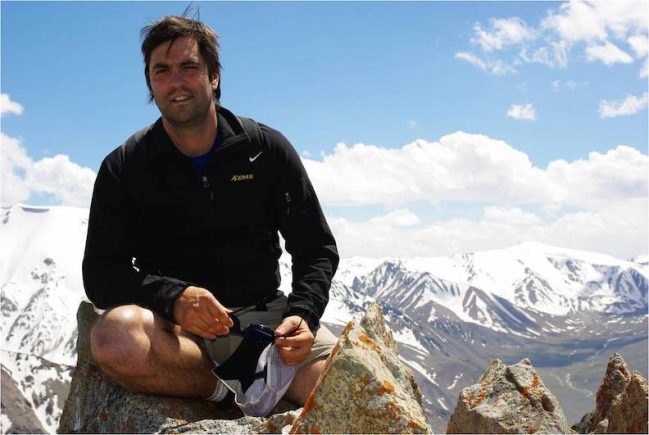 Man sitting on top of a mountain with mountains in background.