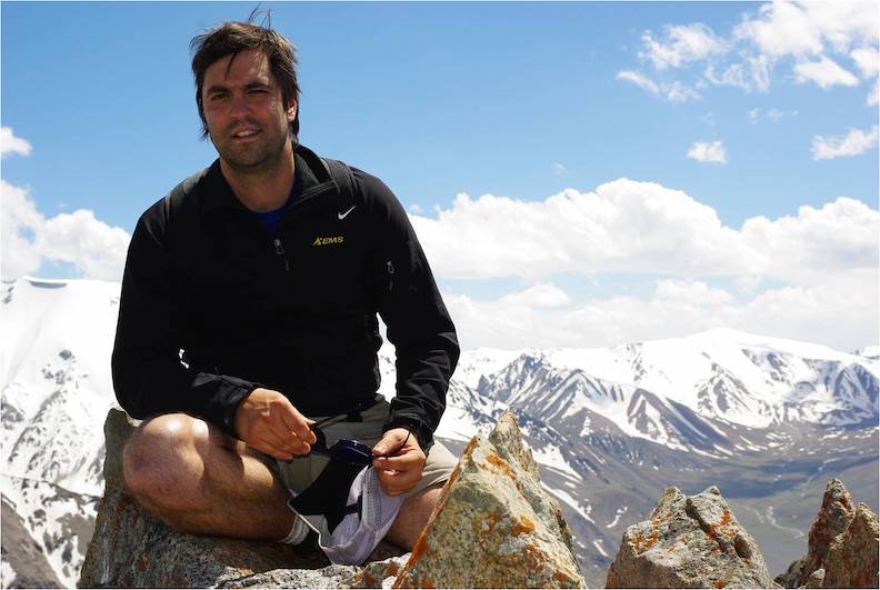 Man sitting on top of a mountain with mountains in background.