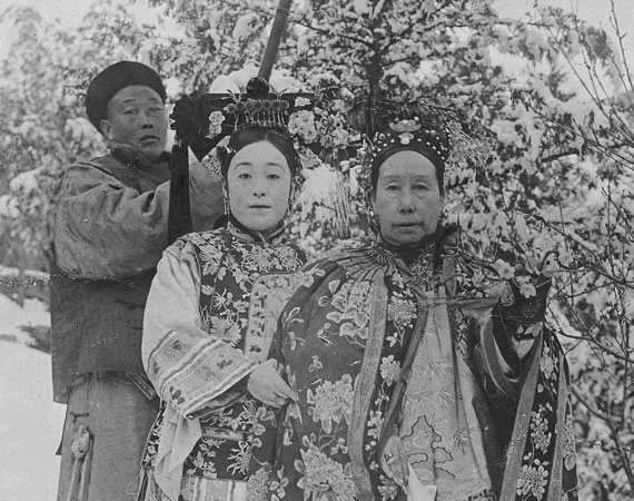 Close up of Cixi in snow with a woman standing to her left, grabbing her robe lightly.
