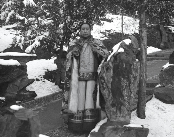 A woman stands among the snowy gardens in a fur robe.