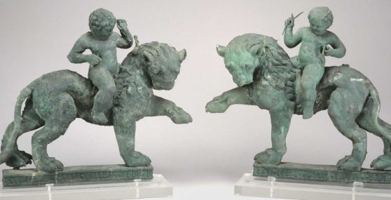 Two statues depicting child-like figures riding lions.