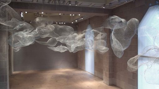 cloudlike formations of wire installed in a stone wall and floor gallery space.