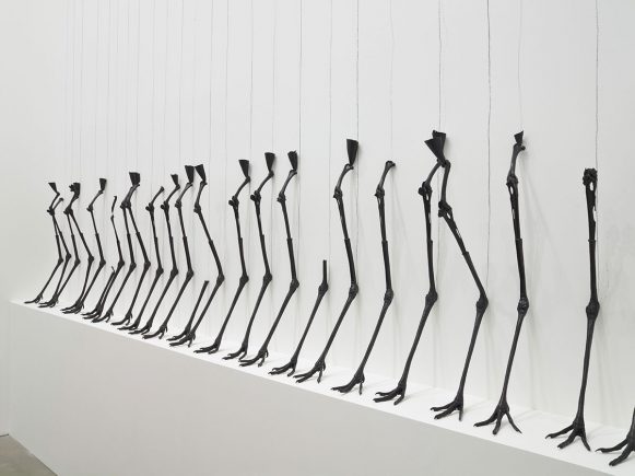 Black cranes' legs, sculpted, detached, against white wall.