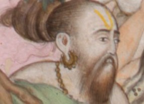 close up of a man with a beard, long hair in a top knot, earrings and a necklace