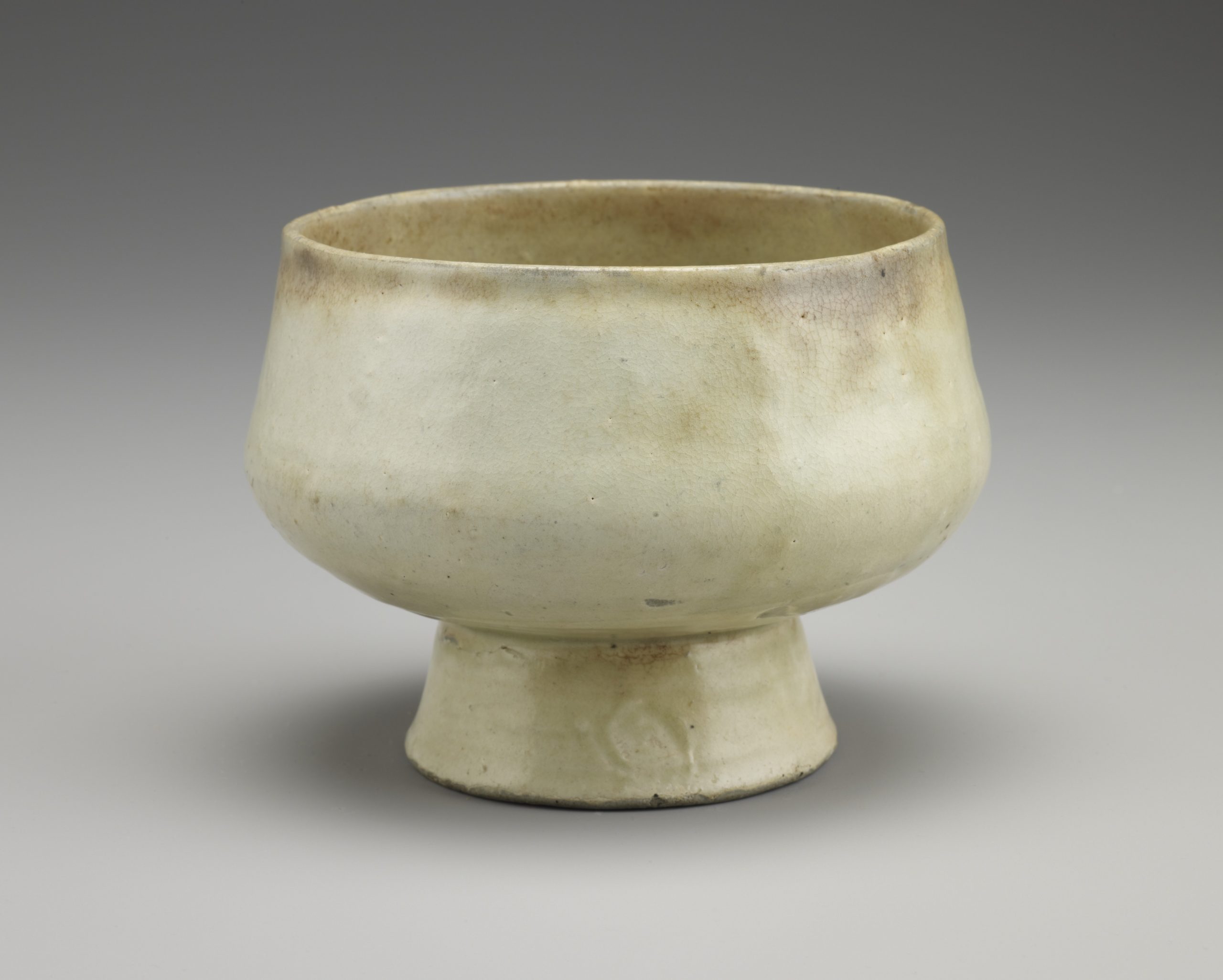 Pale yellow bowl held up on a tall, narrow foot. The inside of the bowl's mouth is a darker, brownish yellow.