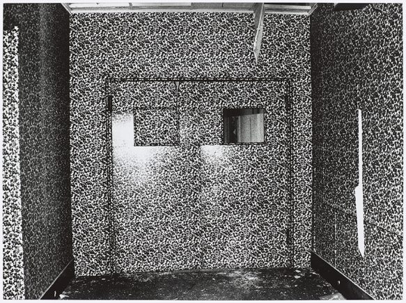 black and white photo of a room wallpapered in busy patterned paper, double doors with windows directly ahead