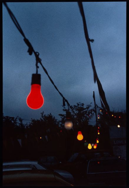 a string of red and yellow lights against a blue sky, trees and the wires dark