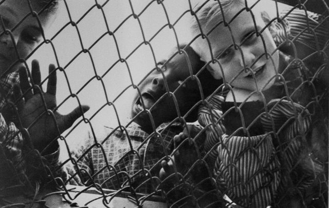 Black and white photo of two children behind a chain link fence