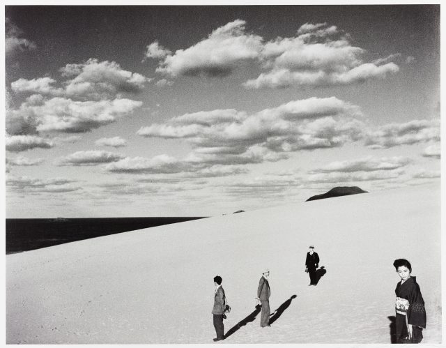 several people working on the dunes with a cloud filled sky behind them