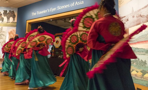 Performers wearing colorful, traditional garments process through a museum gallery.