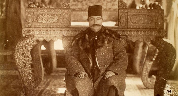 Sepia-tone photograph of a seated man wearing a large coat.