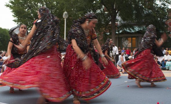 Dancers wearing colorful, traditional garments twirl during an outdoor performance.