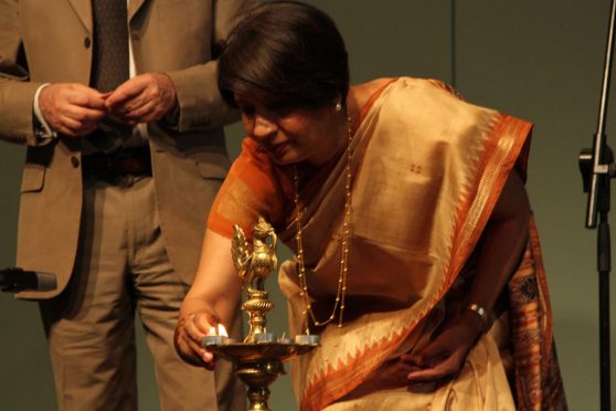 A woman in a yellow-and-orange sari bends over and lights a golden lamp.