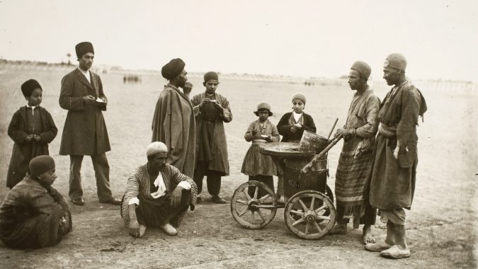 A group of adults and children stand around a wheeled cart in an arid setting.