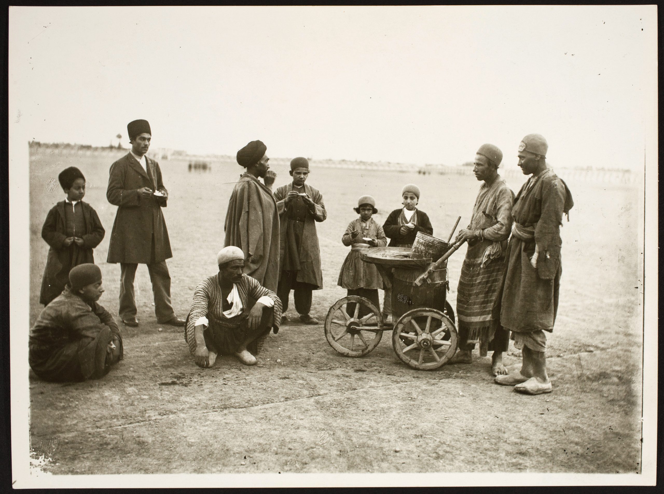 A group of adults and children stand around a wheeled cart in an arid setting.