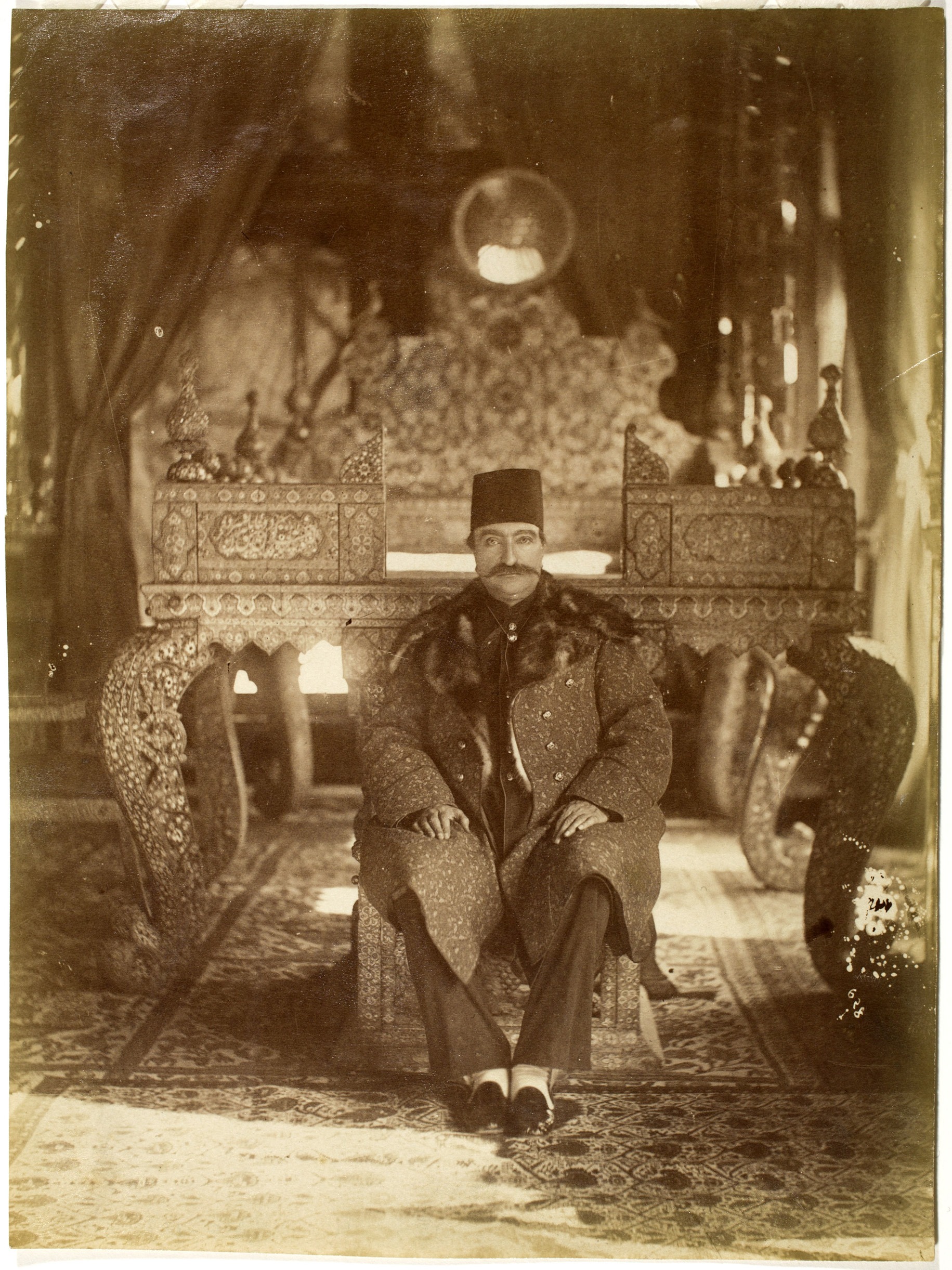Sepia-tone photograph of a seated man wearing a large coat.
