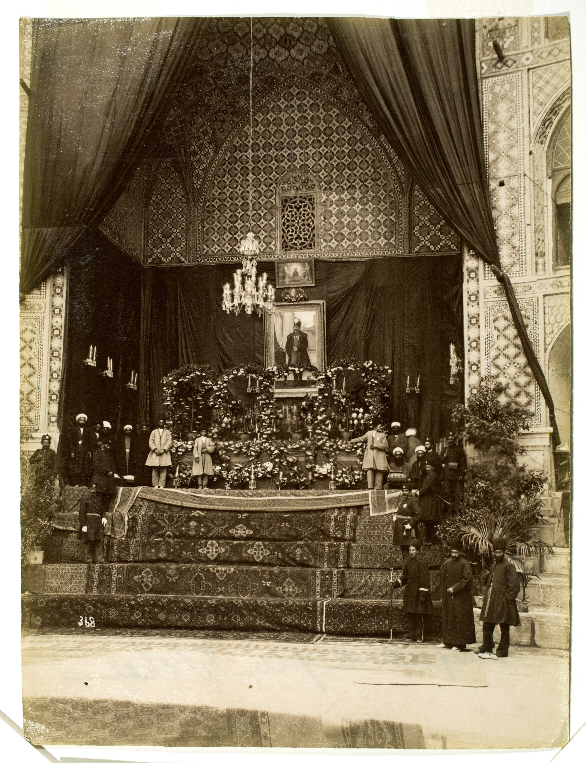 Carpeted steps lead up to a landing where men stand in front of a flower-festooned casket. Above the casket is a portrait of a man.