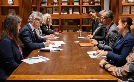 a group of formally dressed people at a long table, one signing a document.