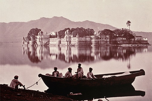 Photograph of a group of men on a boat, looking across a palace on the lake