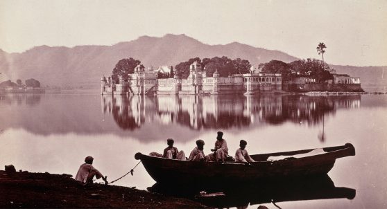 Photograph of a group of men on a boat, looking across a palace on the lake