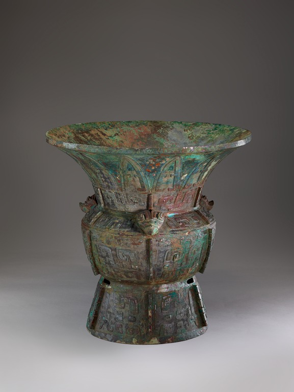 A patinated bronze vessel with a fluted lip, decorated with abstracted, geometric and zoomorphic designs.