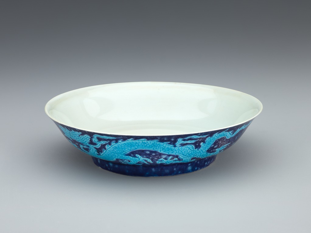 A shallow ceramic bowl with a white interior, decorated on the outside with dark- and light-blue designs of dragons.