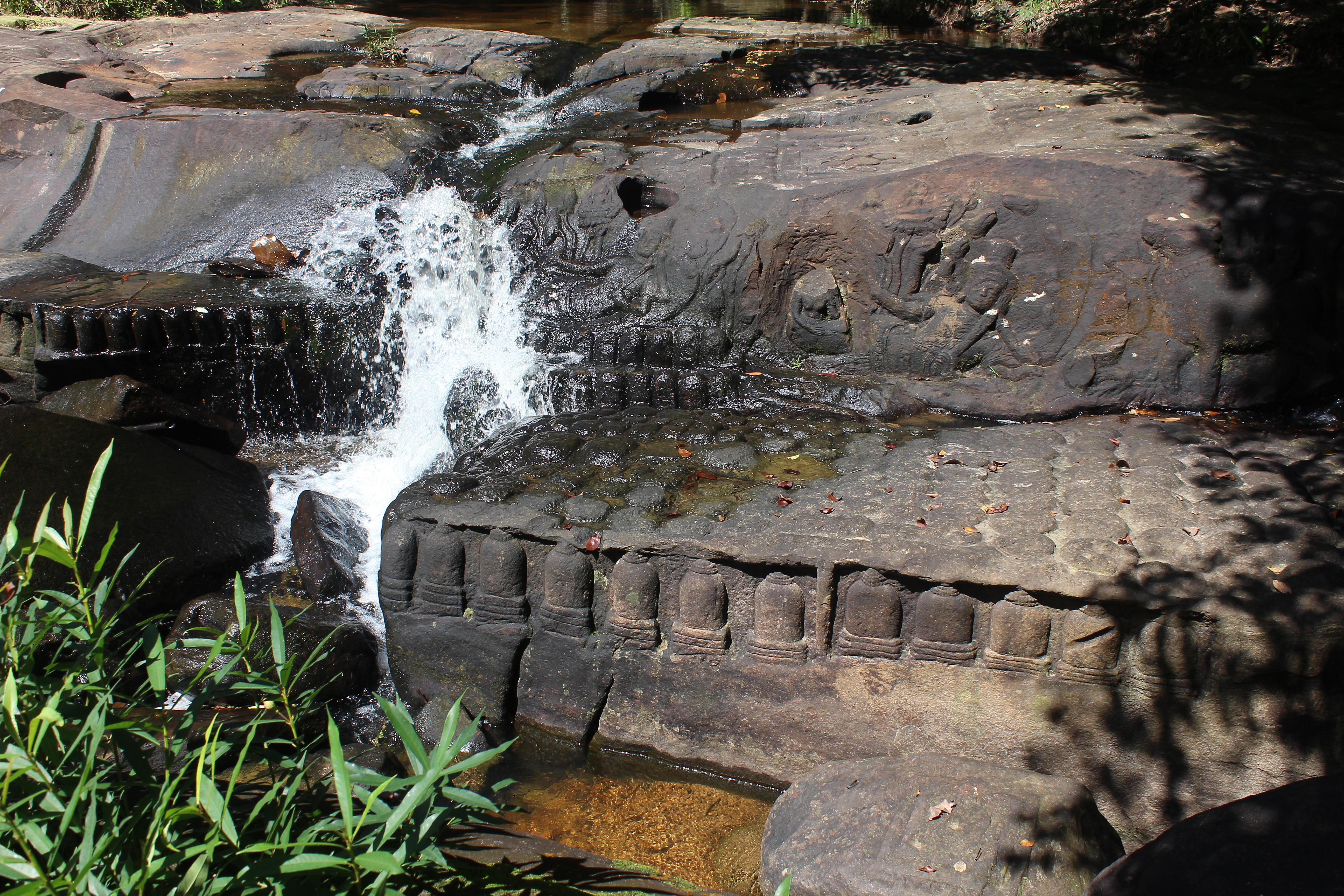 Rushing water over carvings of Vishnu and lingas in the partially dry riverbed