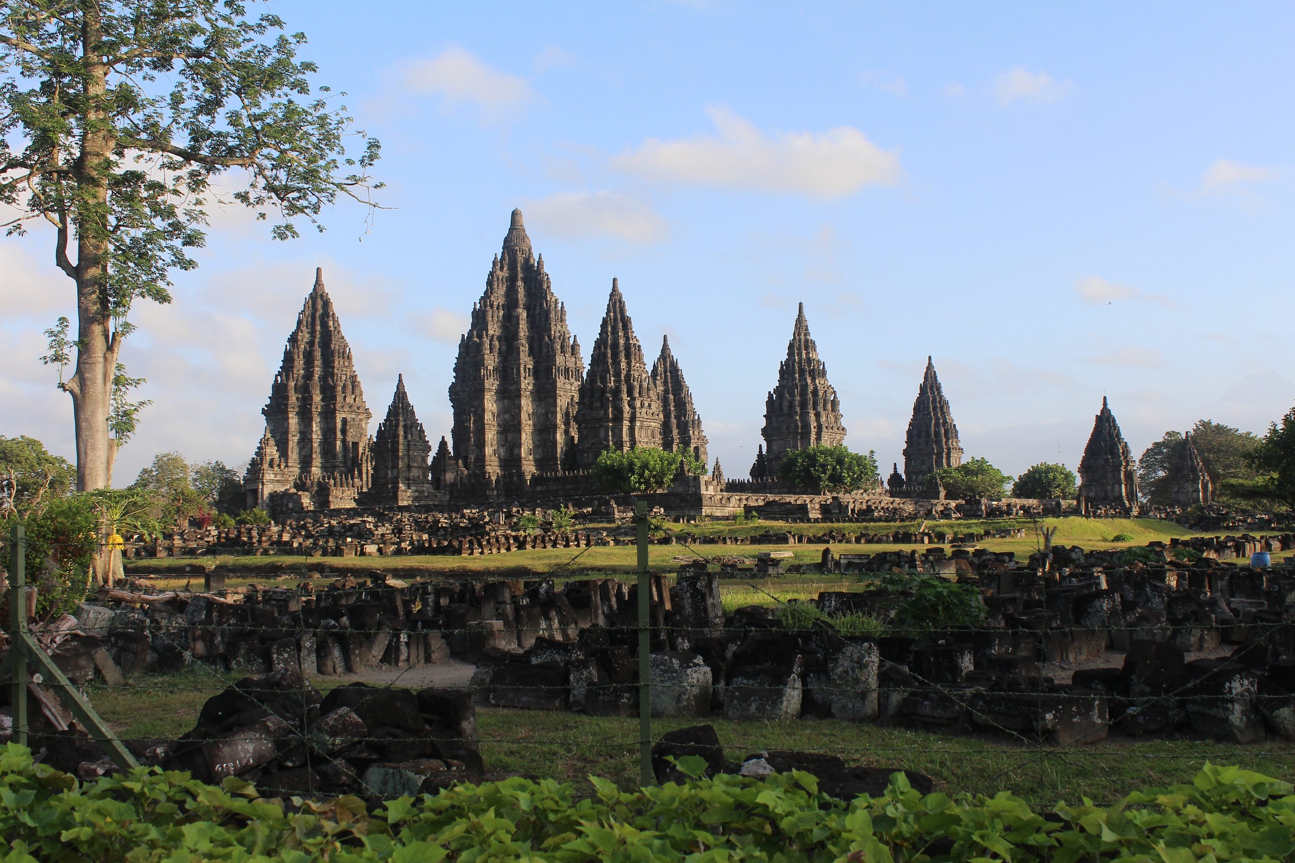 Monumental temple complex with pointed roofs bathed in early morning sun, surrounded by lawn and remains of collapsed shrines