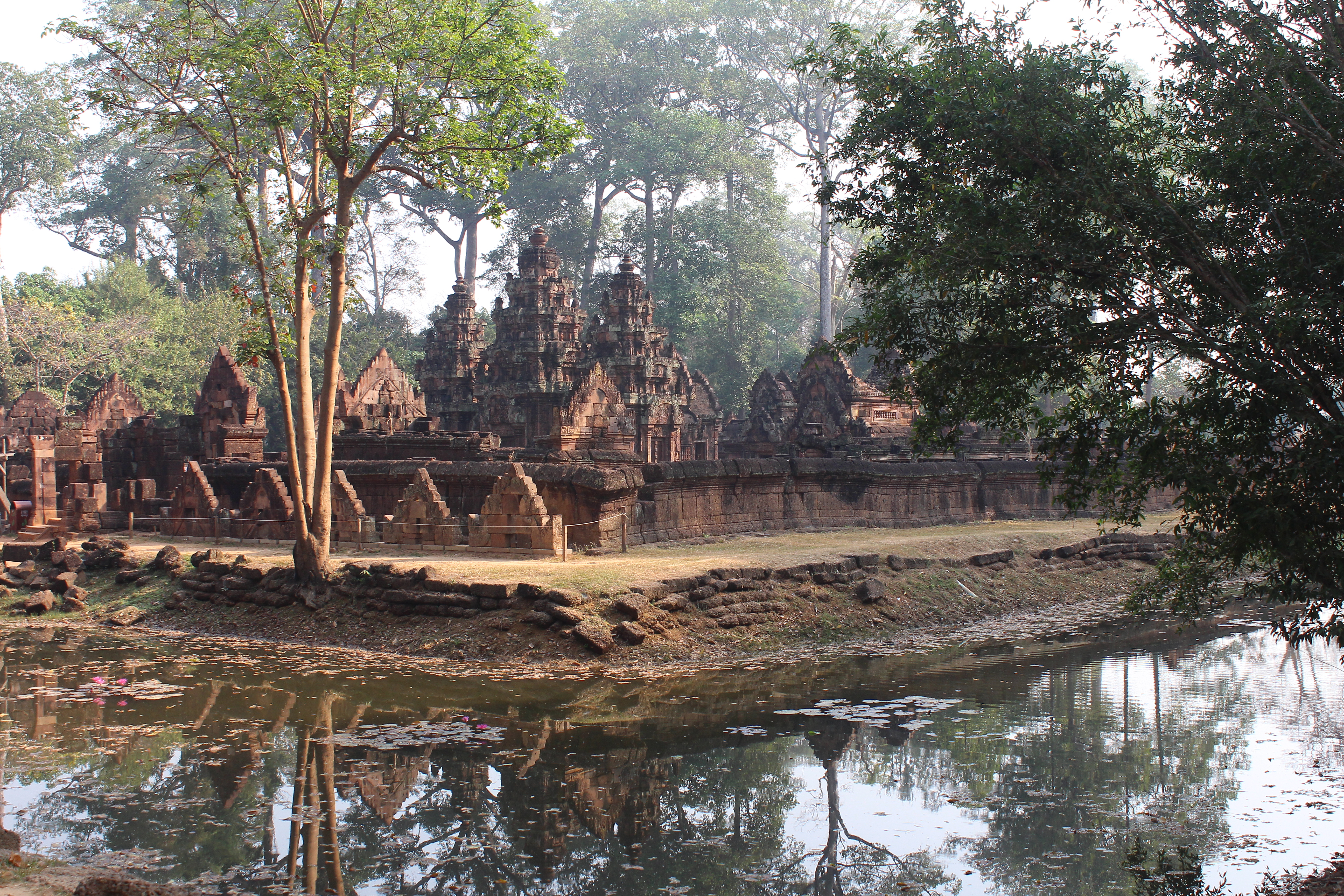 Pink sandstone and laterite temple complex with three central towers, enclosure wall, and moat, seen obliquely