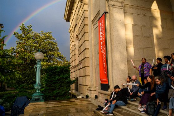 People shelter under the overhang of the Freer steps as a rainbow arcs through the sky above.