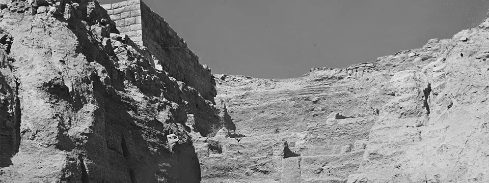 black and white photograph showing cliffs and the edge of a rectangular building with a brick wall