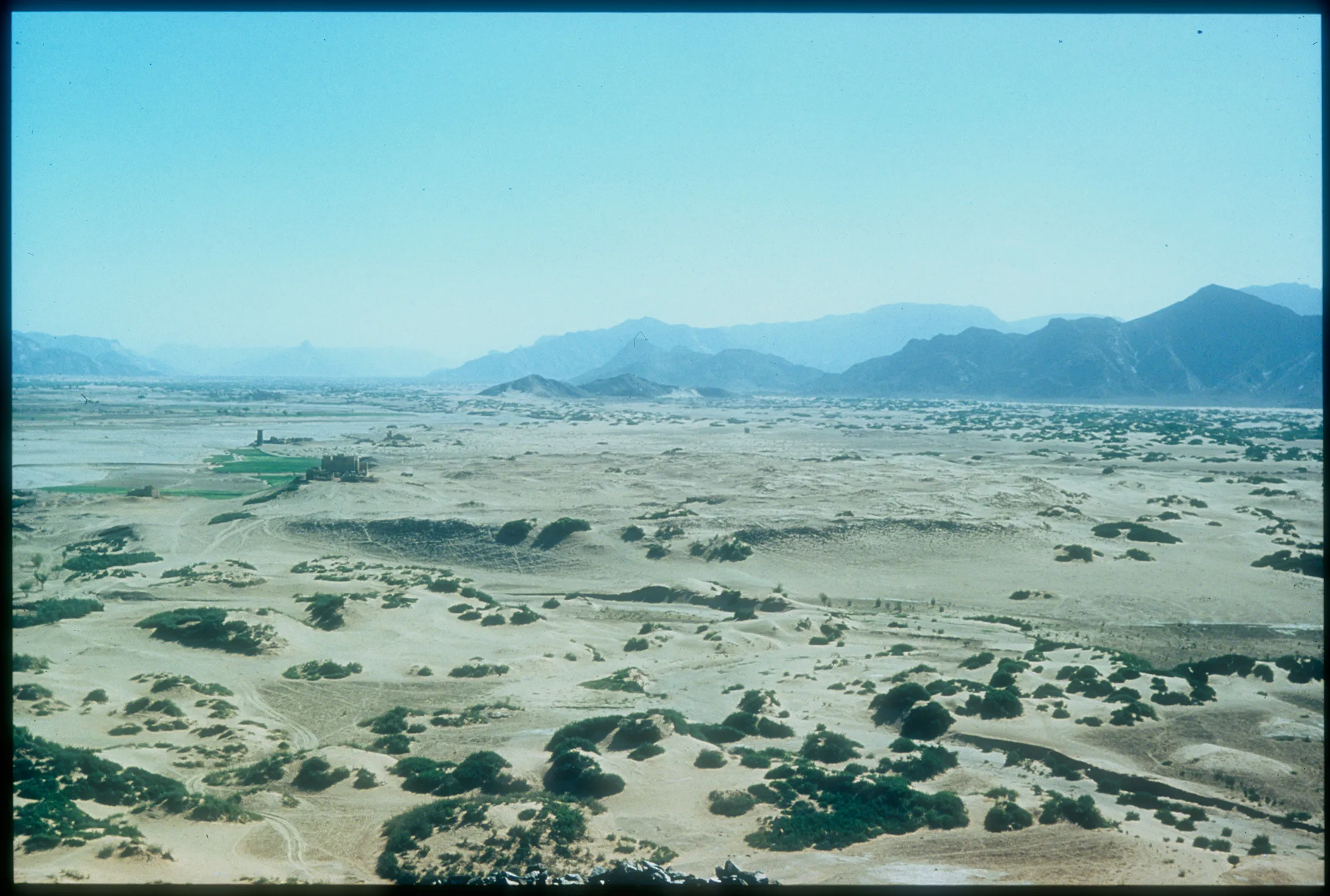 landscape with mountains in the distance and sandy rolling ground dotted with greenery in the foreground