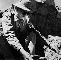 black and white photo of a man in a hat handling an object outdoors